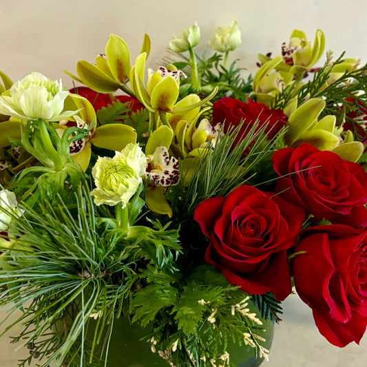 Bouquet of red roses and green orchids in a clear vase on a light background
