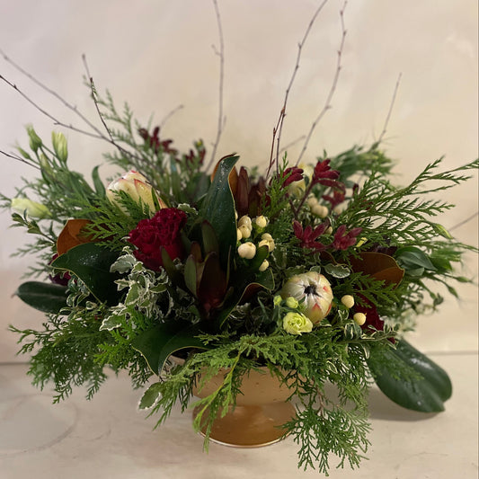 A floral arrangement featuring a variety of holiday-season blooms such as ranunculus and garden roses, in a compote design.